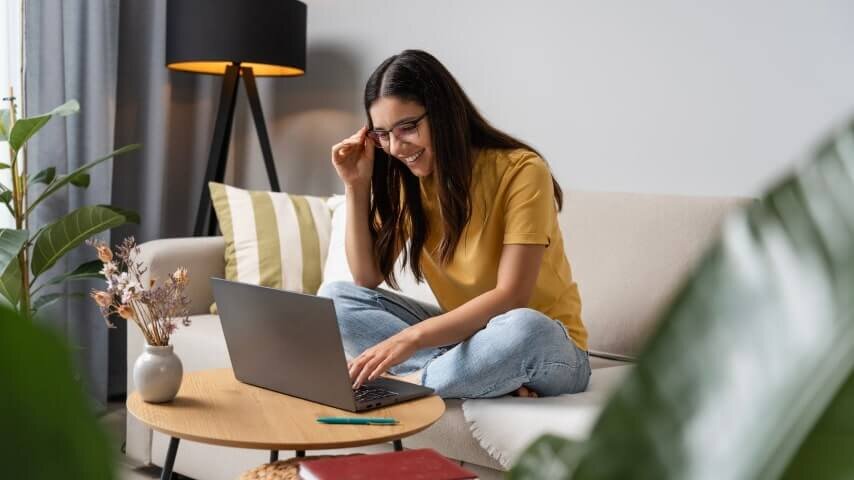 A woman sitting on a couch and looking at her laptop screen.