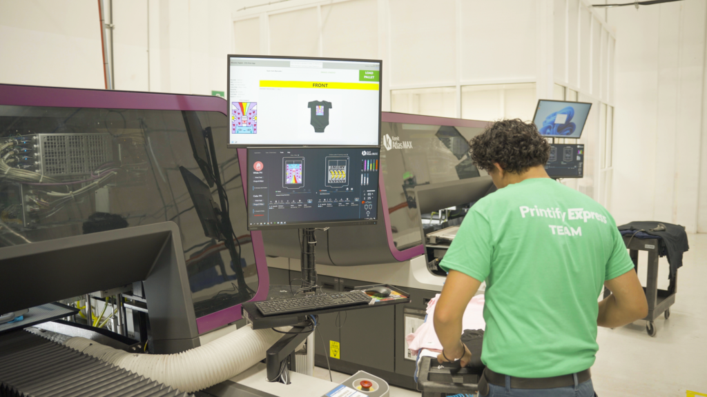 A printing facility worker in a green shirt focused on his work while using a t-shirt printing machine.
