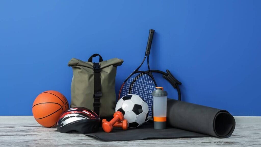 Various sports equipment items placed on the floor – a yoga mat, water bottle, tennis racket, and more.