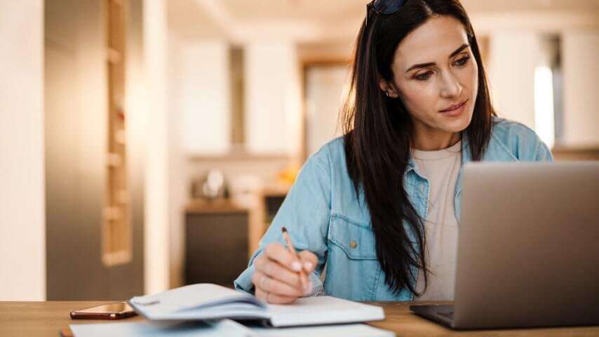 A woman writing down notes in a notepad from a laptop.