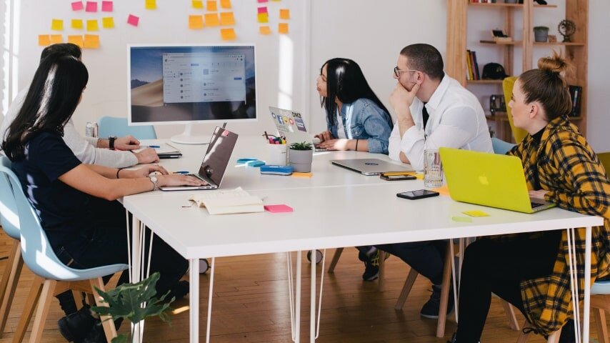 People sitting at the table looking at whiteboard with sticky notes on it.