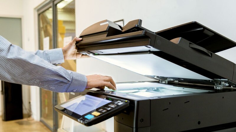 A person using a photocopier opens the lid to place documents for copying.