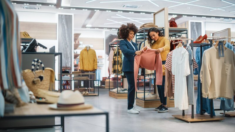Two women in a clothing store examining a pink sweater together.