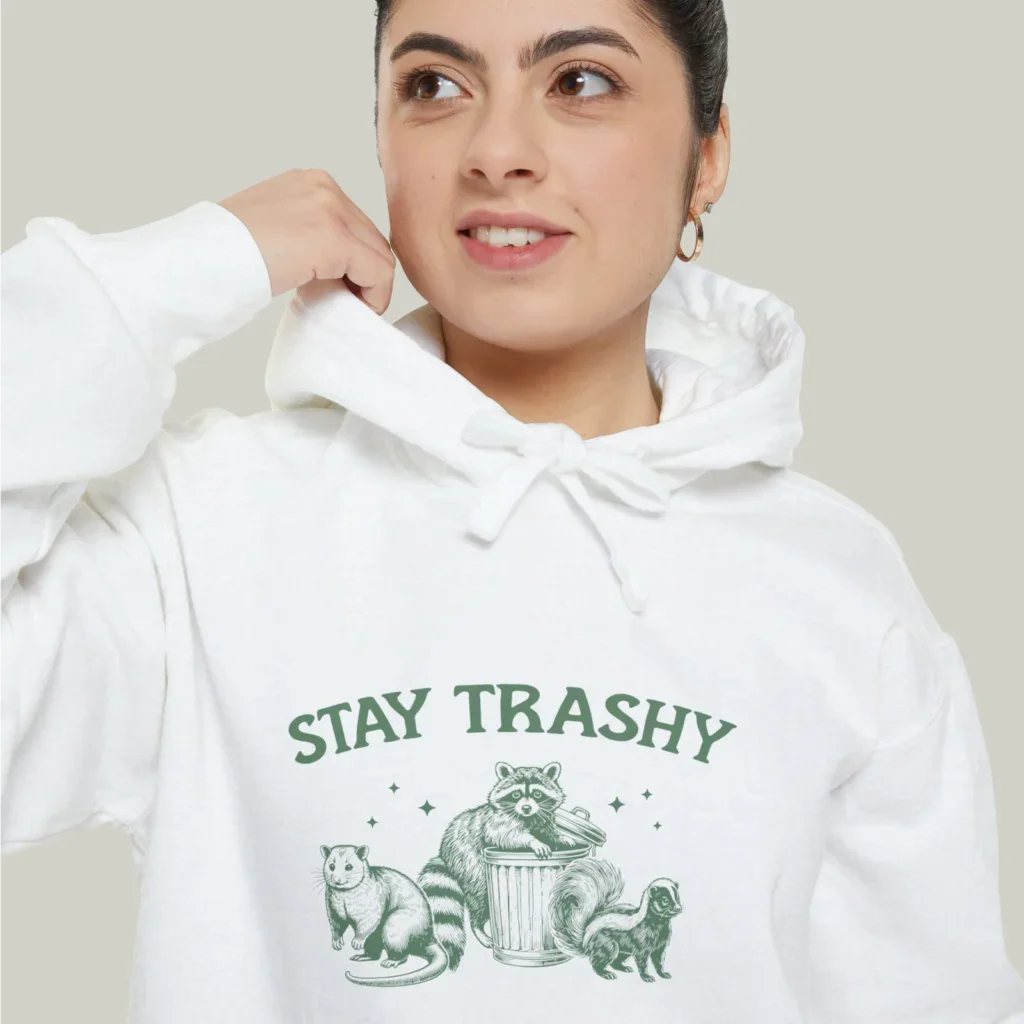 A close-up shot of a woman wearing a white “Stay Trashy” hoodie with an illustrated raccoon and other animals.
