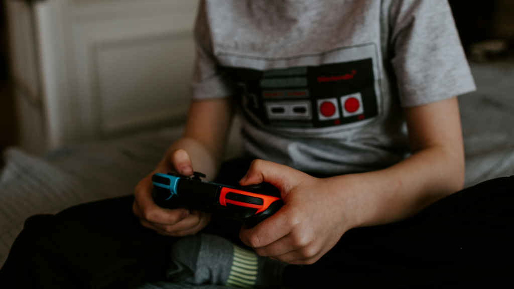 A person in a grey t-shirt with a gaming-themed print of an old game controller, holding a gamepad.