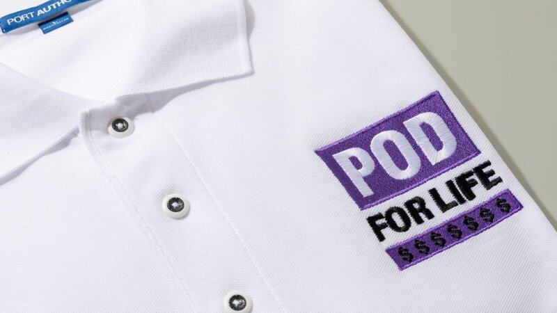 A white polo shirt with the embroidered text "POD FOR LIFE" in purple and black, along with dollar signs.