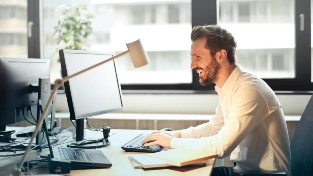 A smiling man looks into a monitor screen.