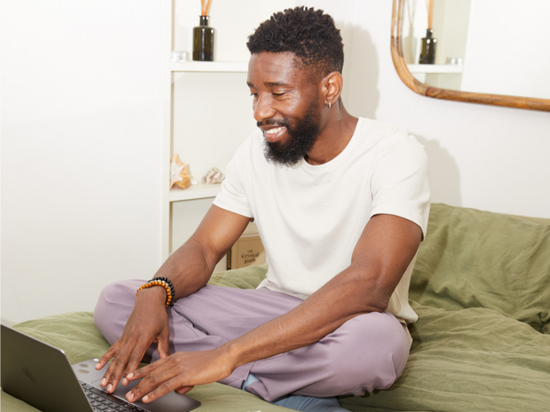 A man sits on a bed with a laptop, brainstorming creative t-shirt design ideas in a cozy setting.