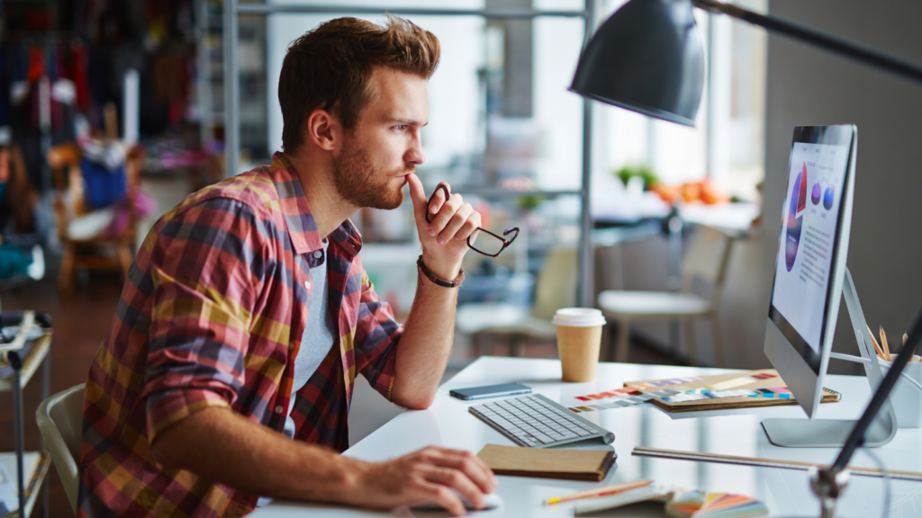 A man looking at a monitor, holding his glasses, and thinking about how to sell SVG files on Etsy.