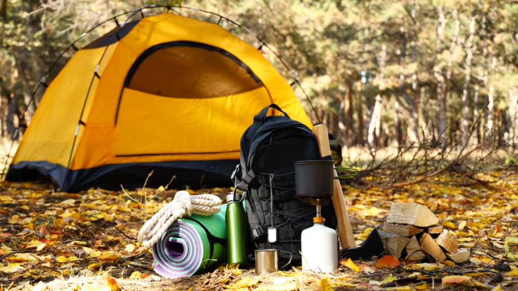A camping scene featuring a tent, a backpack, and essential gear, all positioned on the ground in a forested area.