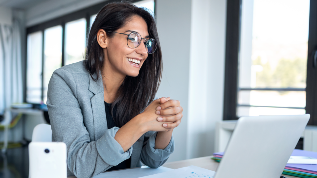 A smiling woman in glasses is using a laptop, showcasing a moment of engagement and productivity.