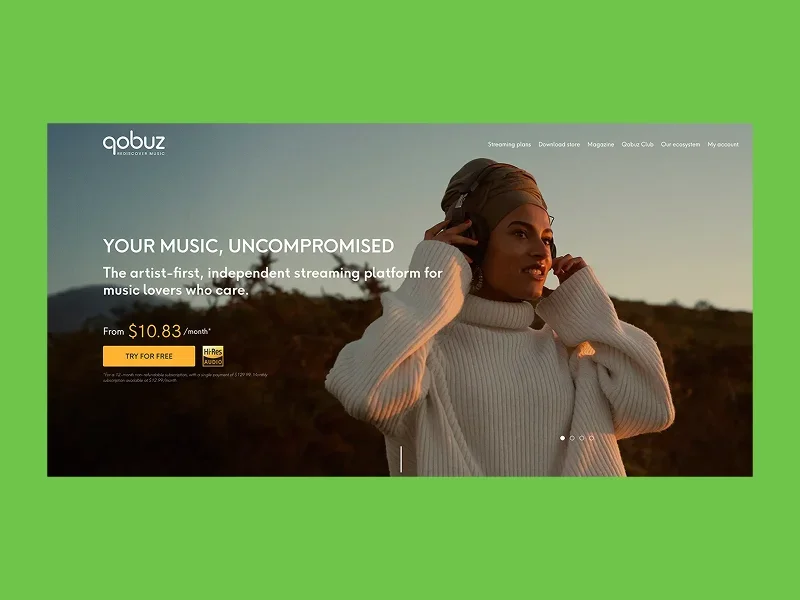 Woman in a cozy sweater enjoys music with headphones against a sunset backdrop.