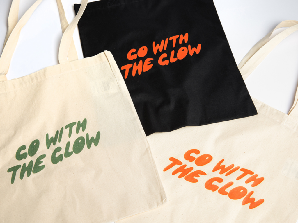 Three “Go With the Glow” custom tote bags in multiple colors.