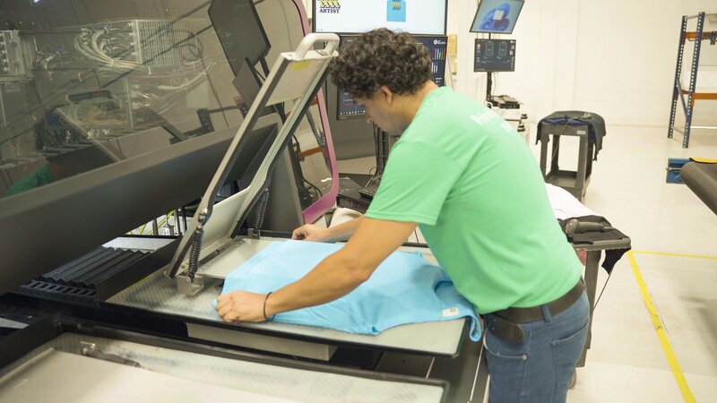 A woman diligently works on a DTF printer, surrounded by tools and materials in a bright, organized studio.
