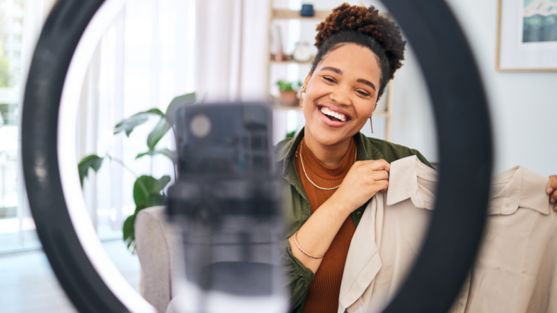 A woman smiles while holding a shirt in front of a mirror, reflecting her joyful expression and the shirt's design.