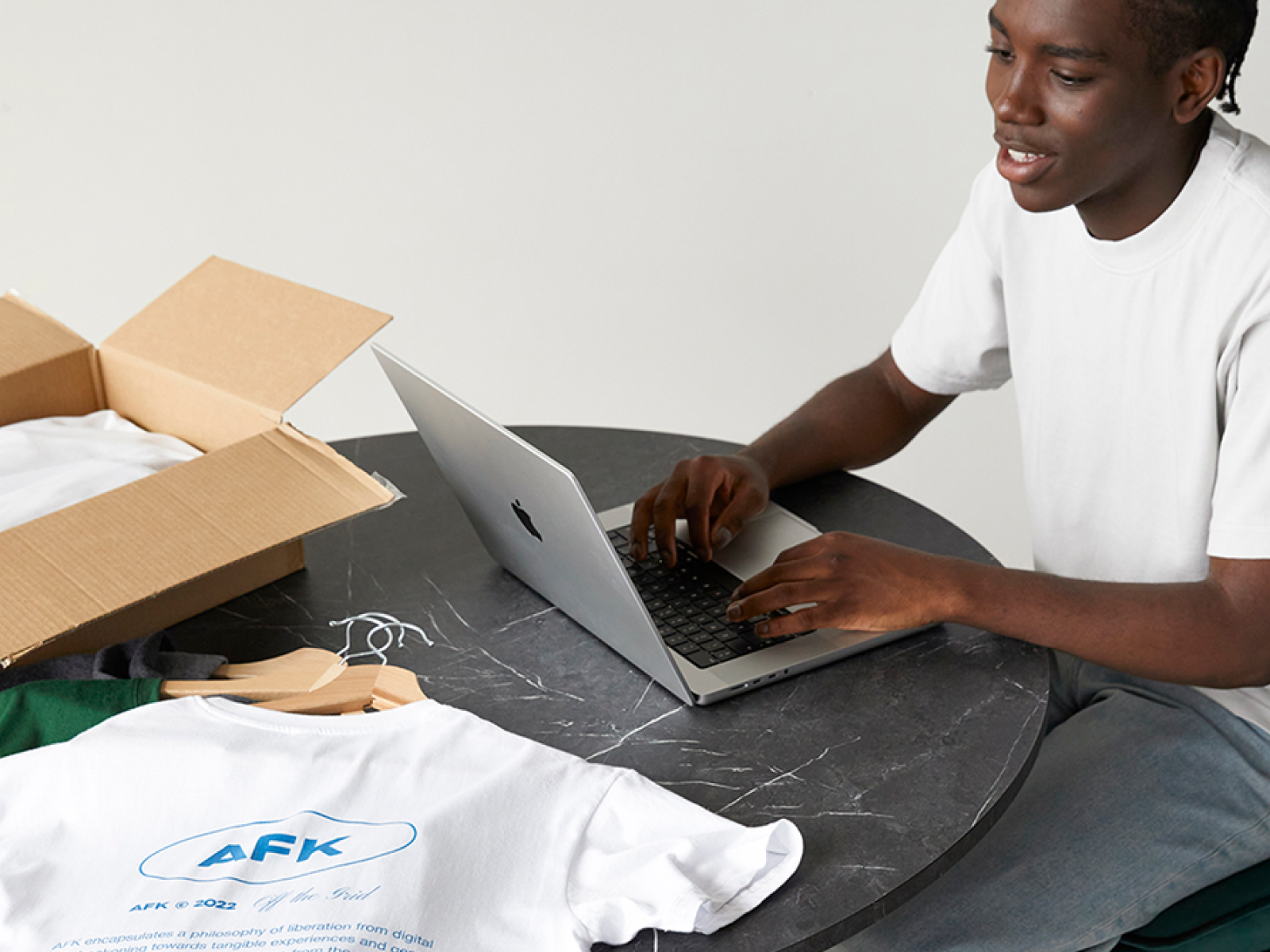 A man sitting at a marble table with dropshipping products on top of it, typing on a laptop.