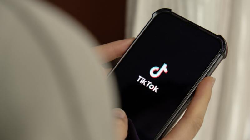 A person holds a smartphone displaying the TikTok logo on a black screen.