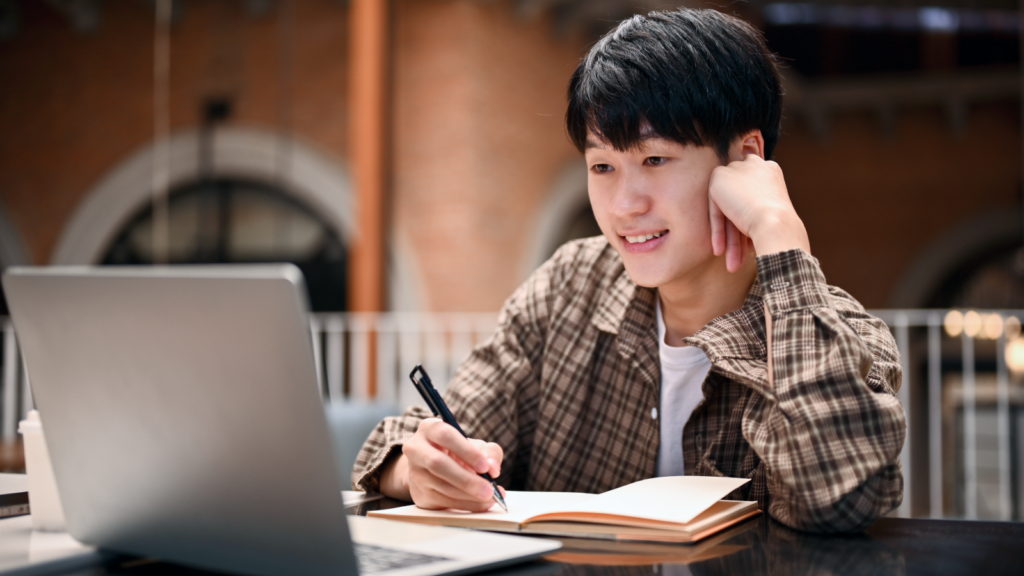 A young man is sitting in front of a laptop, with an open notebook where he makes notes on TikTok affiliate marketing.