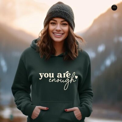 A woman wearing a green hoodie that says "You are enough."