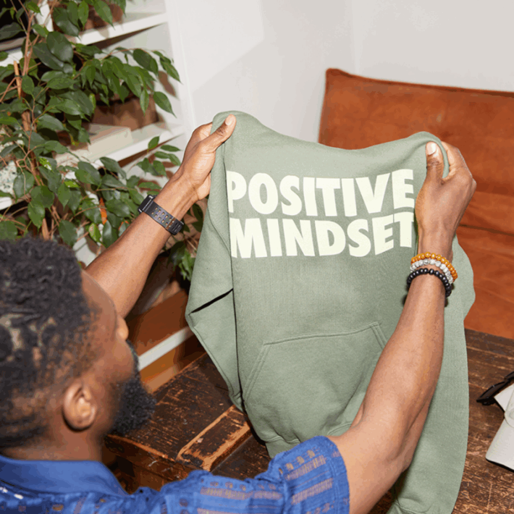 A man is holding a green “Positive mindset” hoodie.