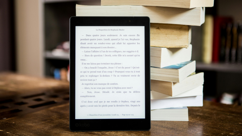 A portable wireless reading device (eBook) placed in front of a stack of books.
