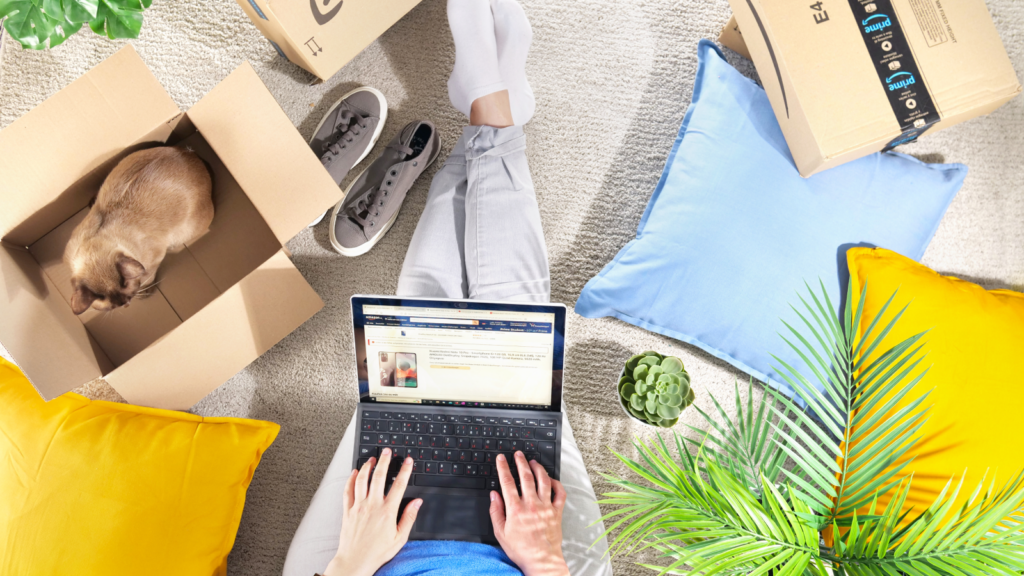 A woman sitting on the floor with a laptop on her lap, surrounded by Amazon delivery boxes.