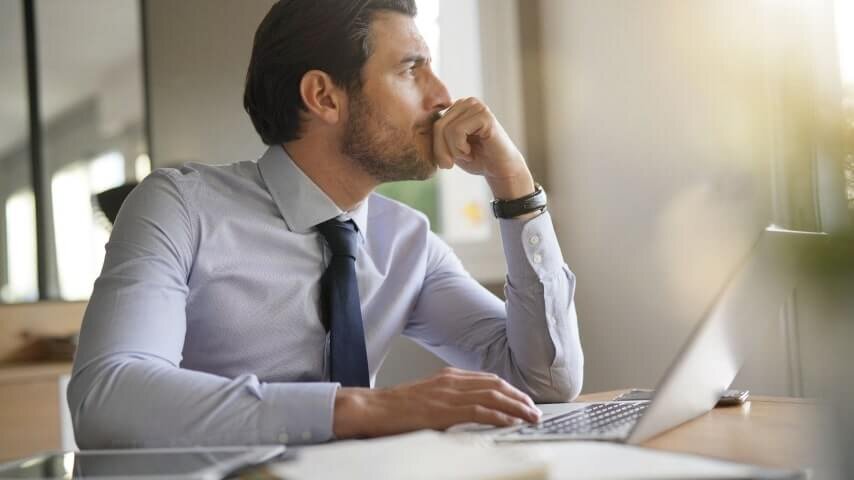 A man sitting by a laptop and looking away while thinking about Etsy ads.