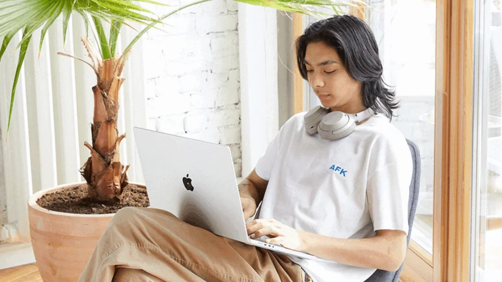 A young man is sitting in a chair with a laptop, selling art on eBay.