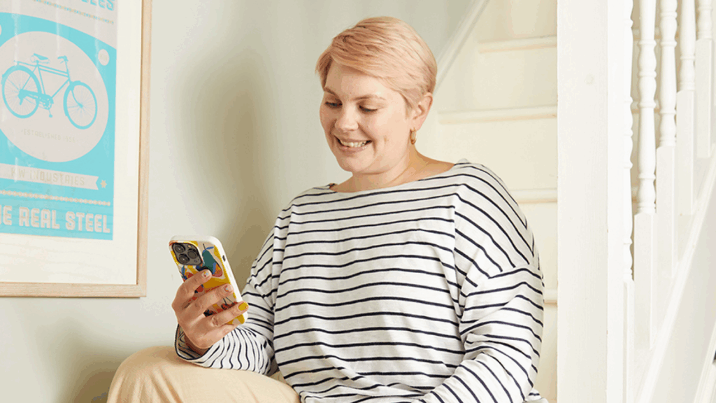 A woman sitting on a stairway, holding a cell phone and looking thoughtfully at the screen.