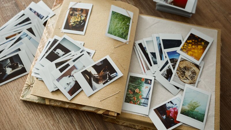 A photo album is open on a table, surrounded by scattered photographs and polaroids.