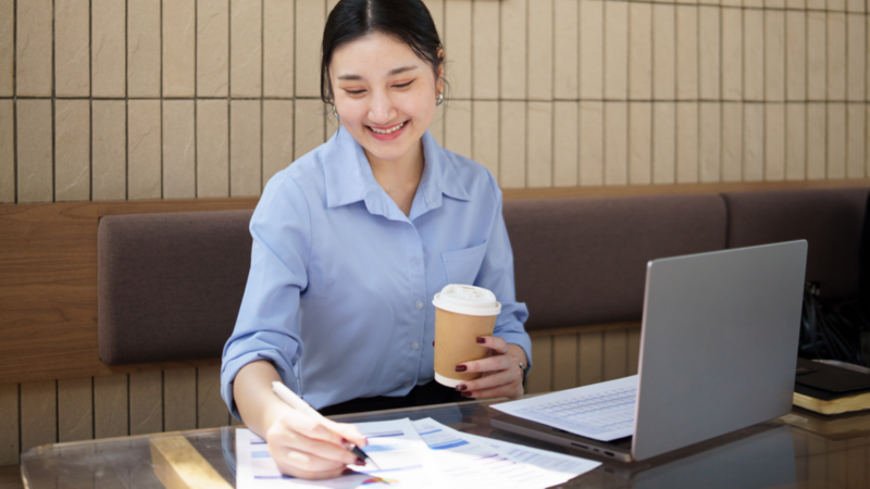 A woman seated at a table, working on a laptop with a cup of coffee beside her.
