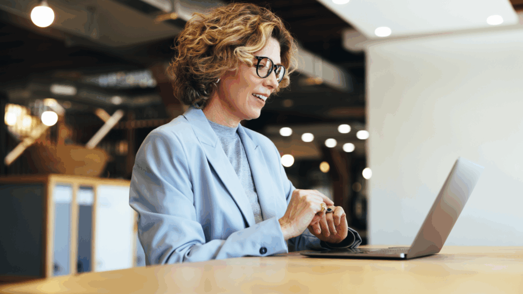 A woman wearing glasses is focused on using a laptop at a desk.
