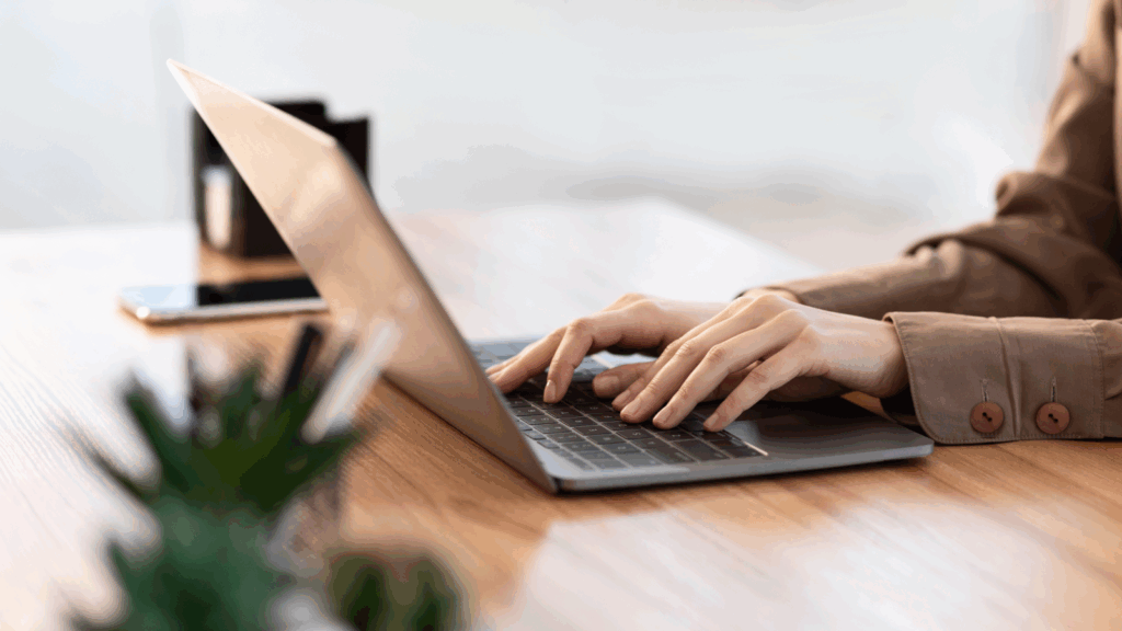 A woman focused on typing on a laptop computer, with her hands positioned on the keyboard.