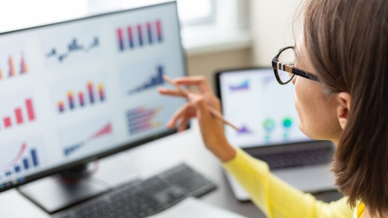 A woman is analyzing data on a laptop screen, with graphs and charts.