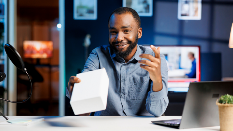 A smiling man holds a white box during a product presentation recording in a film studio.
