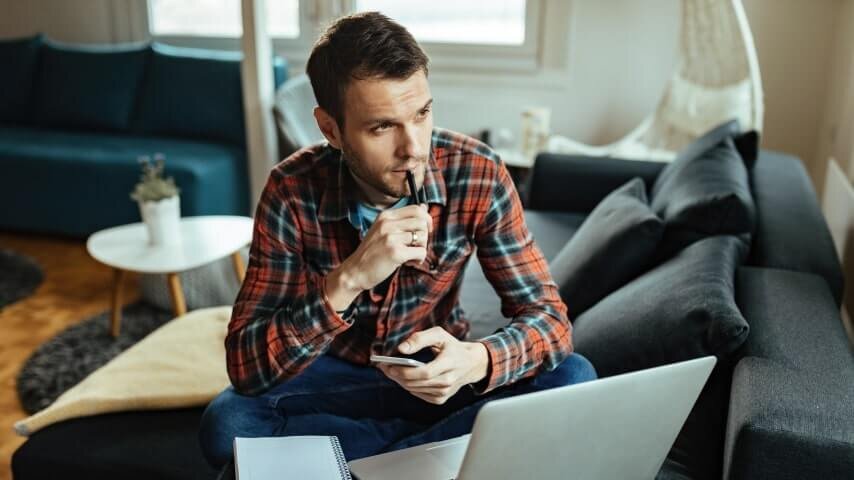 A man sitting by a laptop, looking forward and thinking about how to find suppliers.