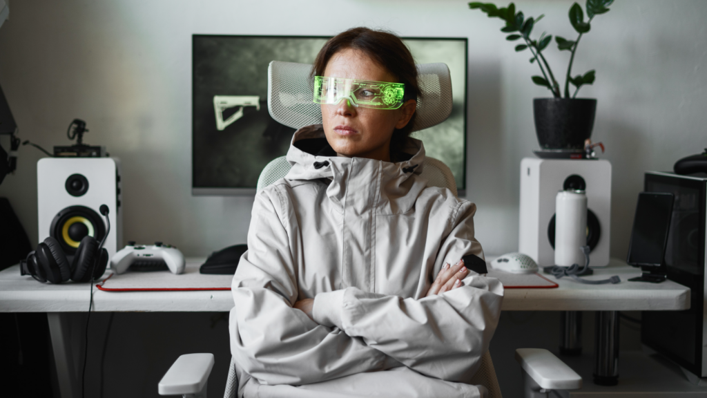 Woman in futuristic green visor, seated with arms crossed. Surrounded by tech, speakers, and a plant in a modern workspace.