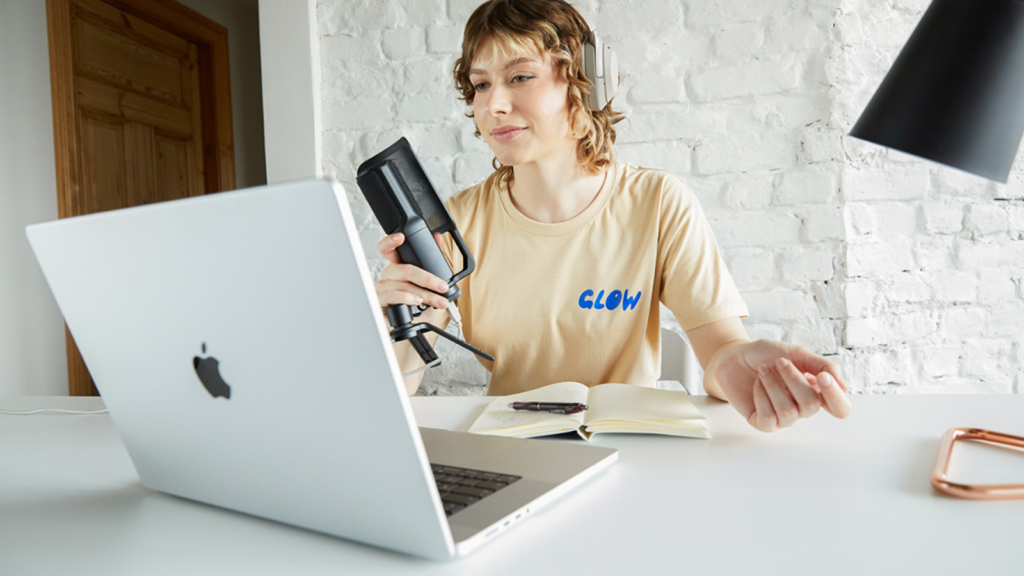 A woman in headphones sitting in front of a laptop, holding a microphone in her hand.