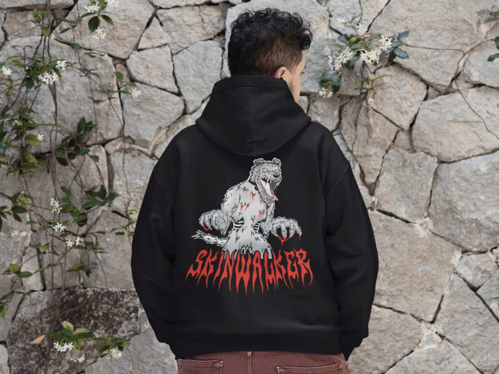 A young man wearing a black “Skinwalker” hoodie on a rockwall background.