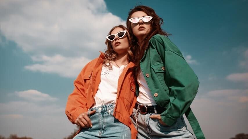 Two women posing while wearing sunglasses and fashionable outfits.