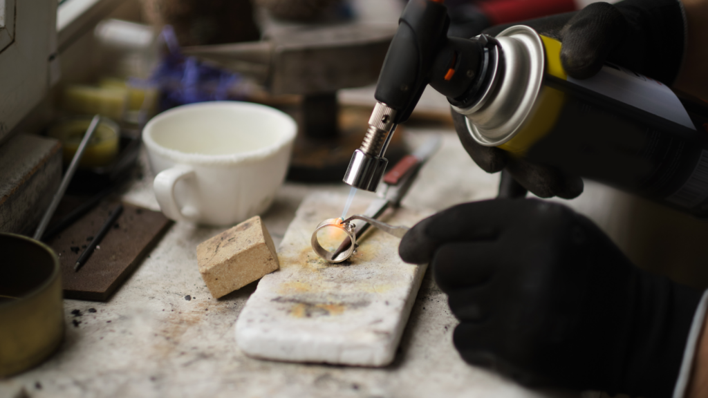 An individual applies a torch flame to a metal piece, showcasing the process of heating for shaping or welding.