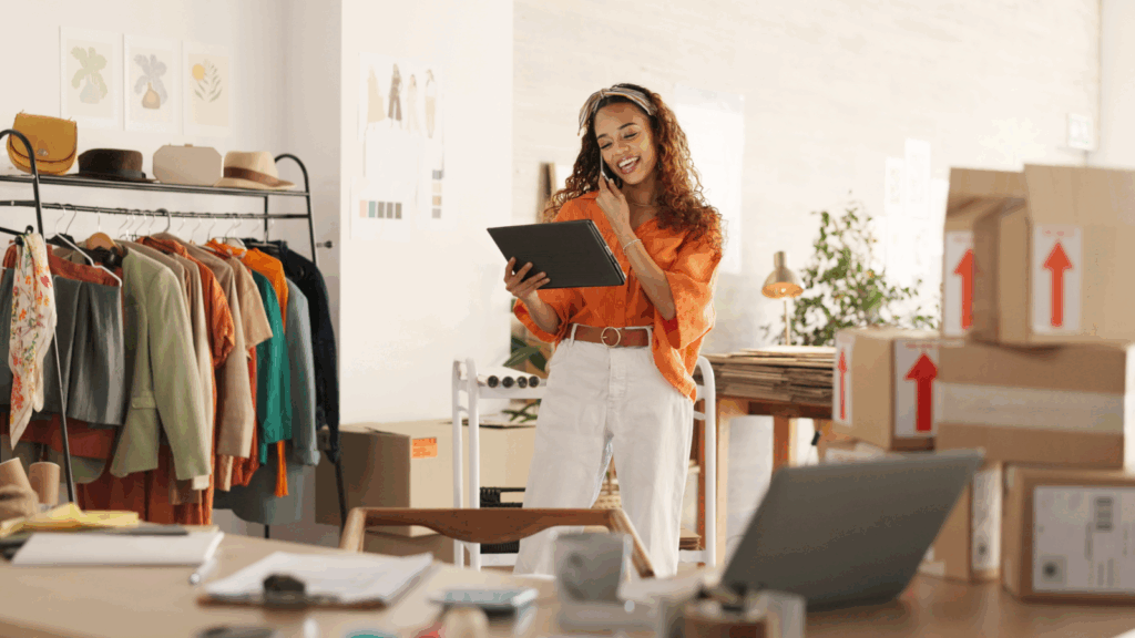 A woman stands by a desk cluttered with boxes and a laptop, appearing focused on her work.