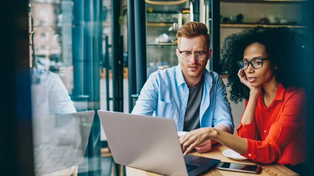 A pair of people at a table, collaborating or working together on a laptop, showcasing teamwork and technology.