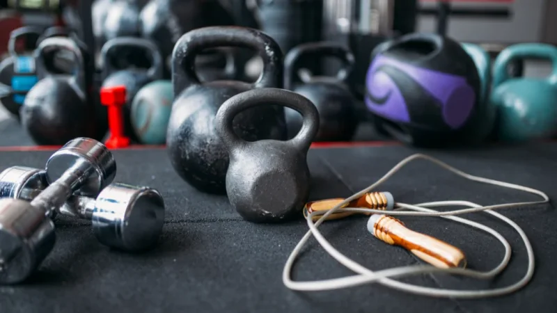 A selection of kettlebells and dumbbells arranged on a black surface, showcasing various weights and sizes.