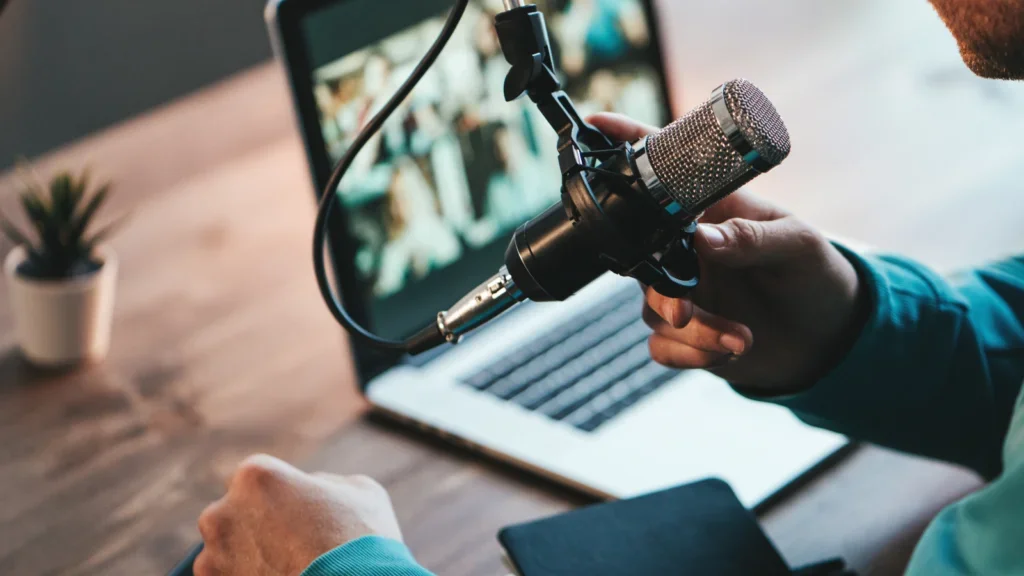 A man holding a microphone and recording his voice using a laptop.
