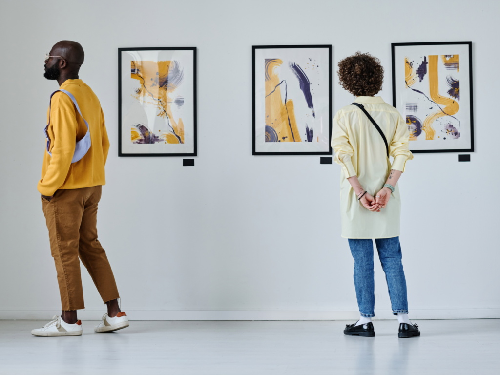 Two people admiring artwork in a bright, spacious art gallery filled with various paintings.
