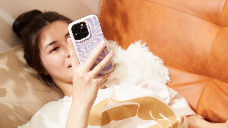 A woman lying on a couch, holding a smartphone and looking at the screen, searching for business shirt ideas.