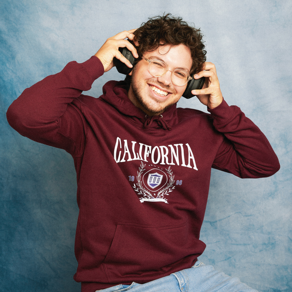 A college student wearing a custom-printed hoodie, listening to music and smiling.