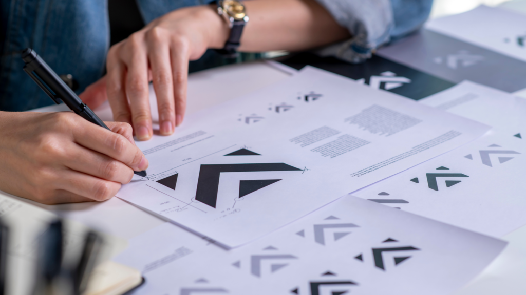 A person reviewing documents featuring various black and white logos on a desk.