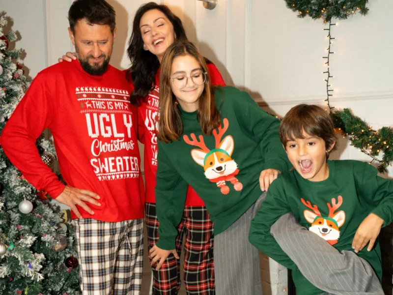 A family wearing red and green Christmas-themed hoodies in a festive environment.